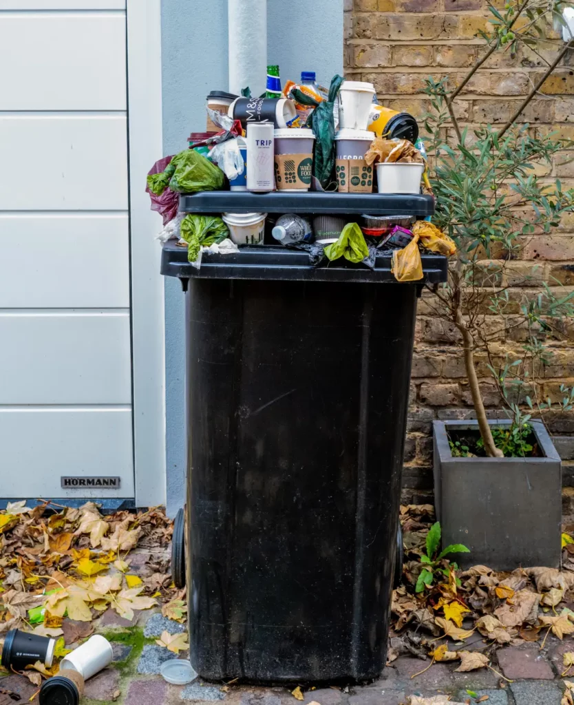 Poubelle débordante de déchets devant une maison