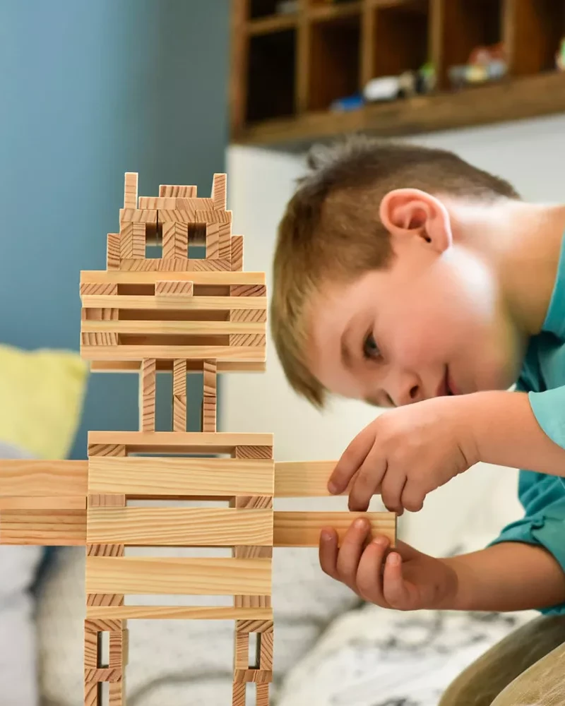 Enfant réalisant une construction avec des planchettes en bois Kapla